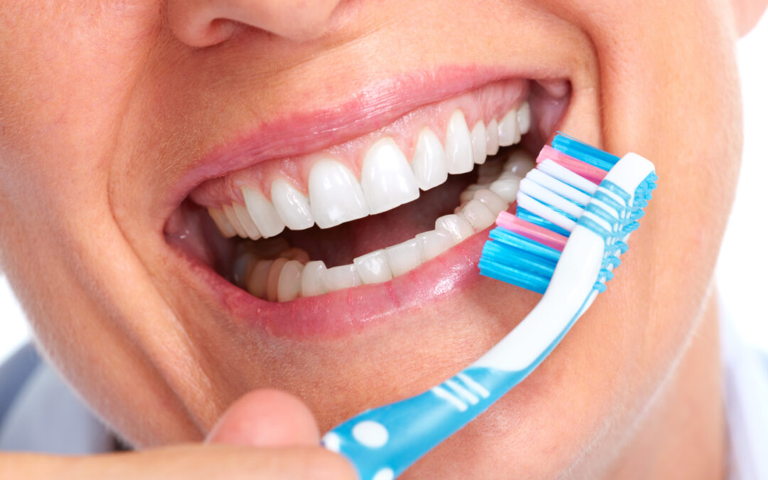 Frau lächelt und hält eine Zahnbürste vor Ihre Zähne, um Ihre Zahngesundheit zu repräsentieren